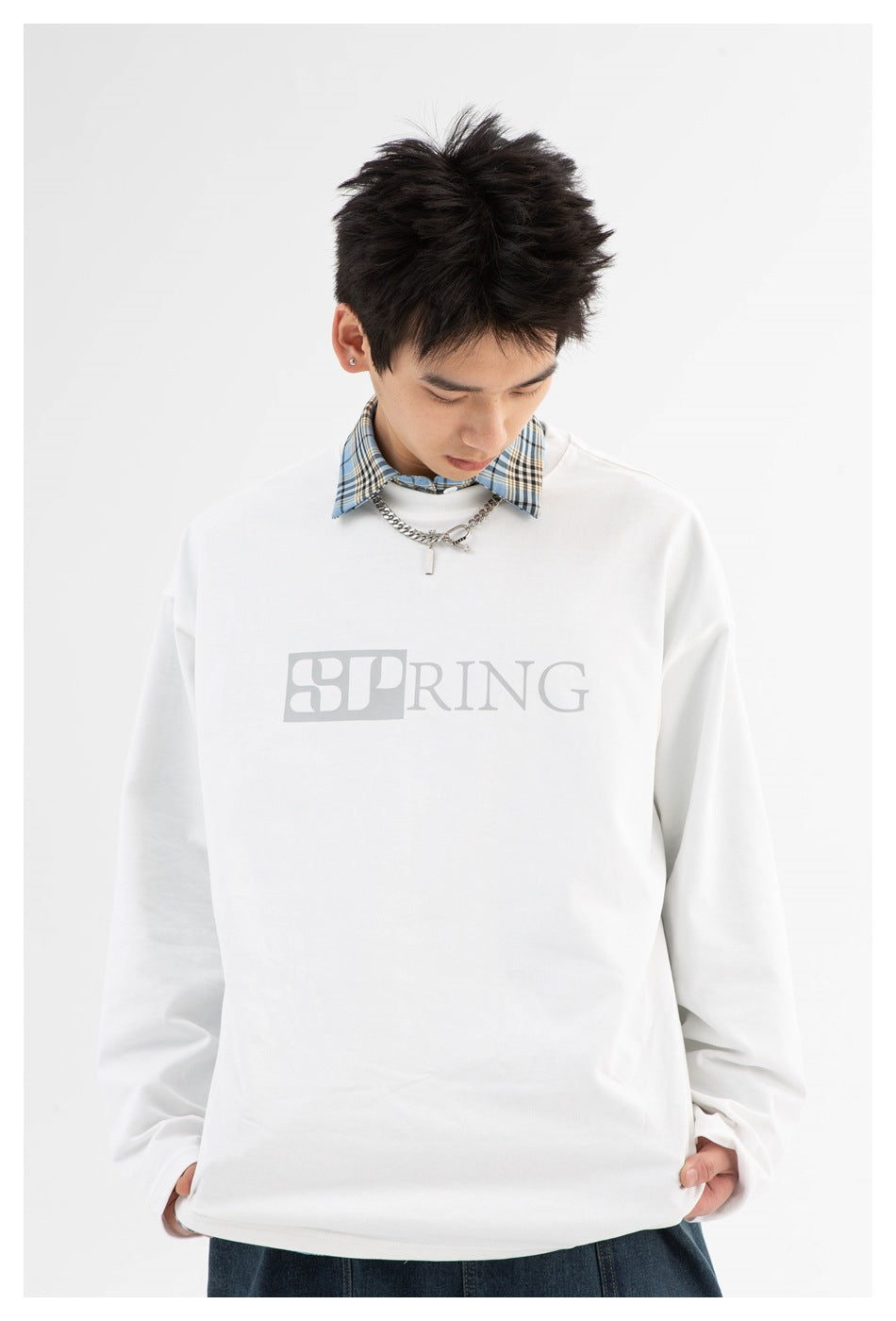 Model wearing a white oversized long-sleeve top with pale gray SPRING lettering and a blue plaid collar.