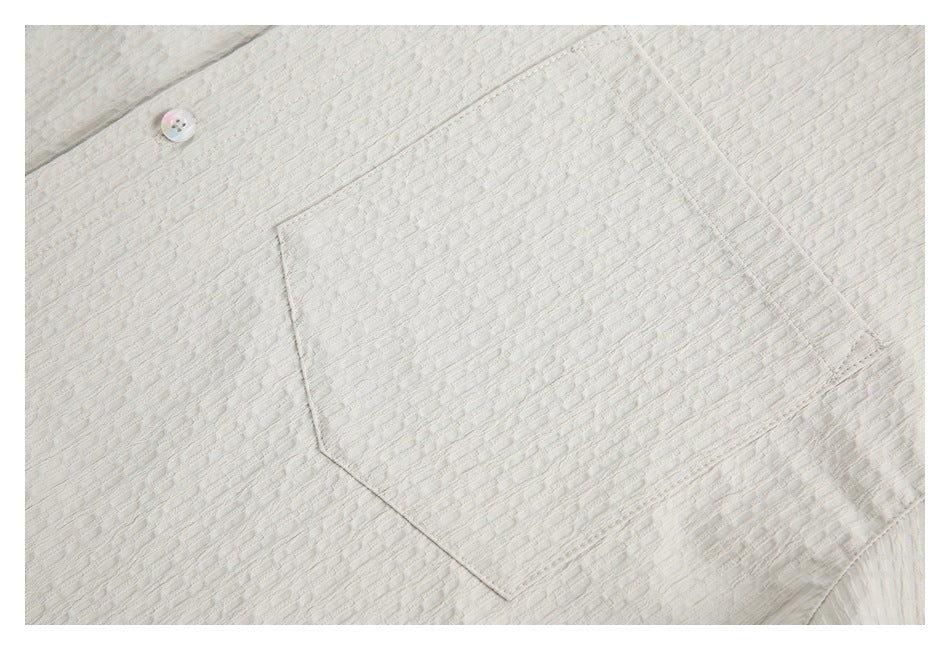 Close-up of an ivory textured shirt's chest pocket and one iridescent button.