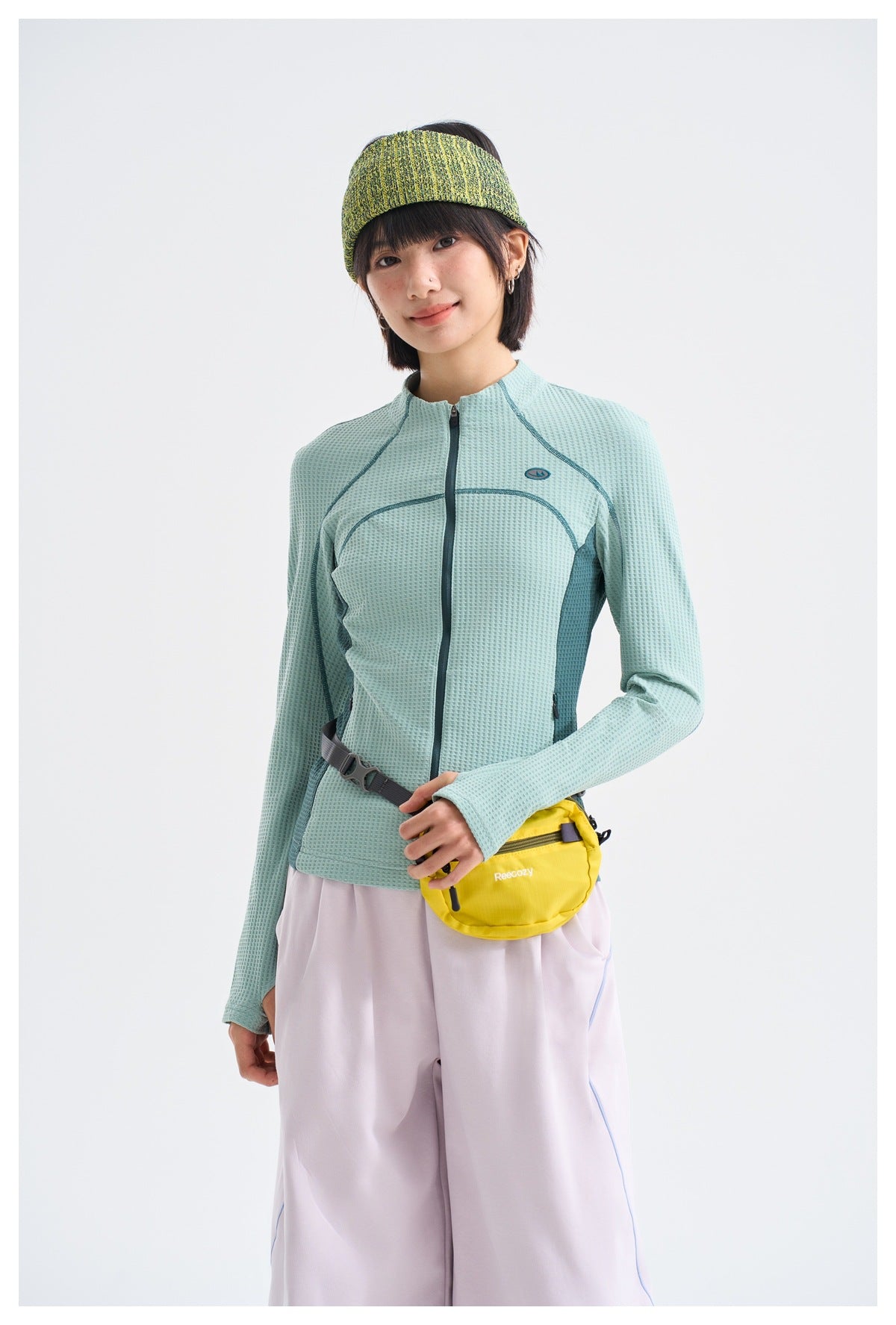 Model wearing the lake green waffle-textured full-zip jacket with a headband, yellow crossbody bag and light pants