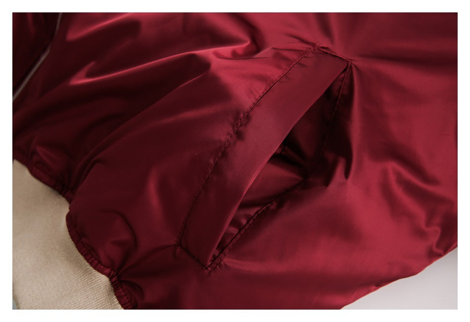 Close-up of a burgundy bomber jacket's slanted welt pocket and beige ribbed cuff.