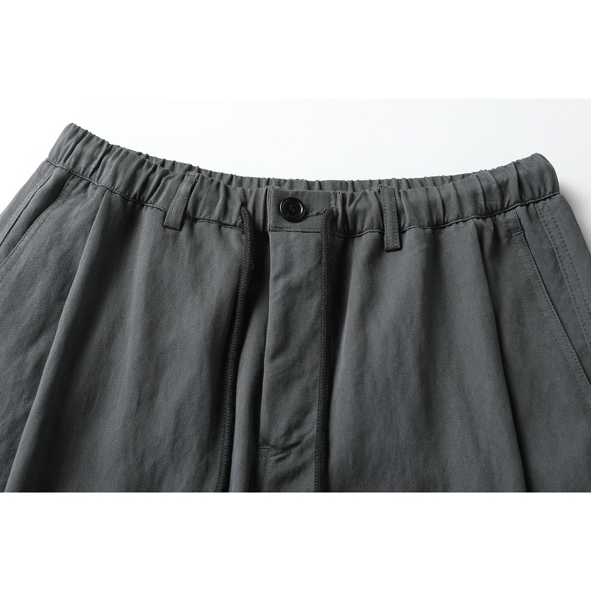 Close-up of charcoal gray trousers showing an elastic waistband, button, belt loops, drawstring, and front pockets.