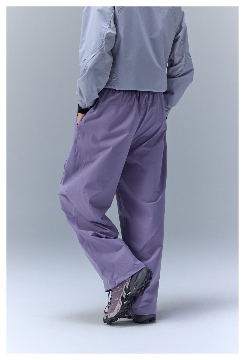 Back view of a person wearing loose lavender pants with an elastic waist and a light gray jacket.