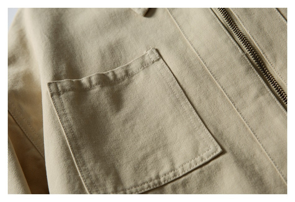 Close-up of a beige jacket's rectangular patch pocket beside the brass zipper.