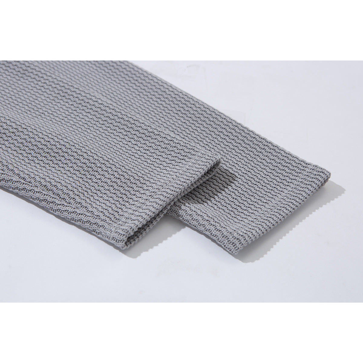 Close-up of the light gray pullover's textured fabric and long sleeve cuff.