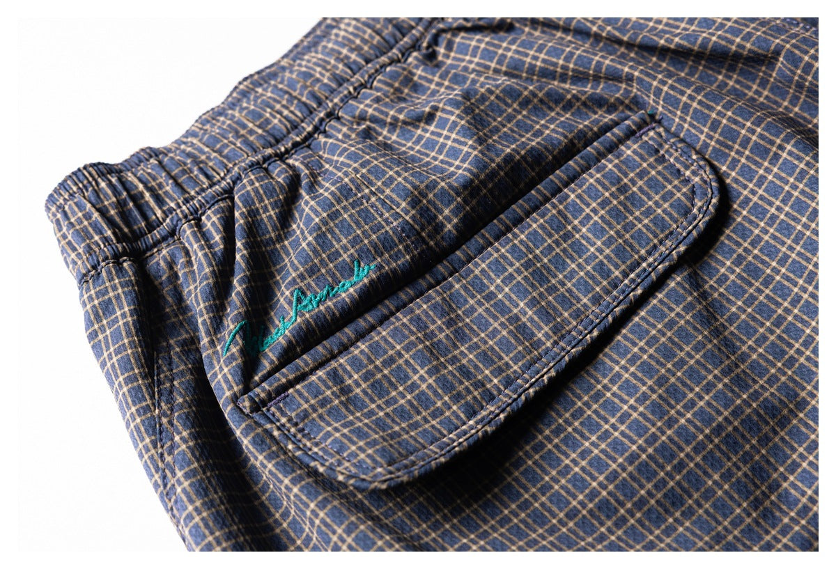 Close-up of a flap pocket and teal embroidery on navy shorts with a tan plaid pattern.
