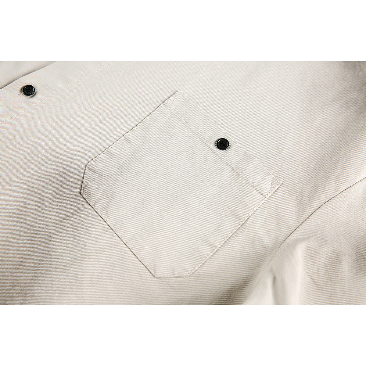 Close-up of a light beige shirt's stitched chest pocket and black buttons.