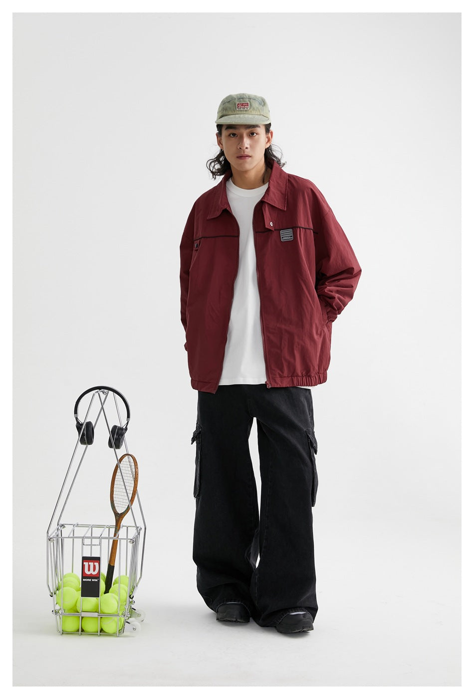 Model wearing a burgundy zip jacket with black trim, white shirt, black cargo pants and sage cap; full-length studio view.