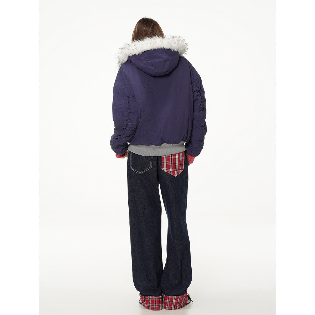 Back view of model in a navy jacket with a white fur-trimmed hood and dark jeans with red plaid details.