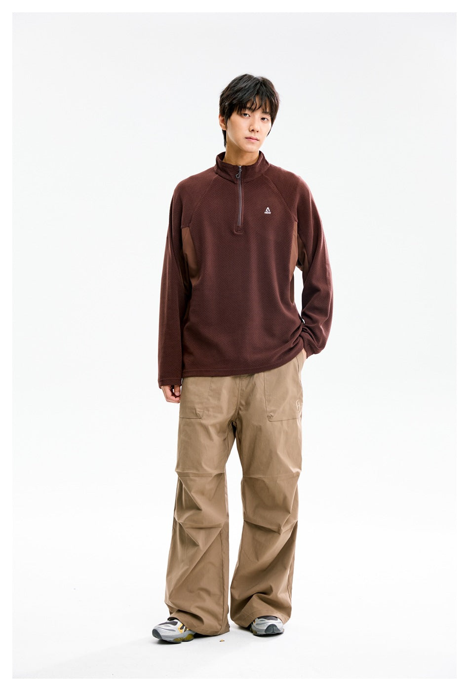 Model wearing a burgundy quarter-zip pullover with brown side panels and loose tan pants, front view.