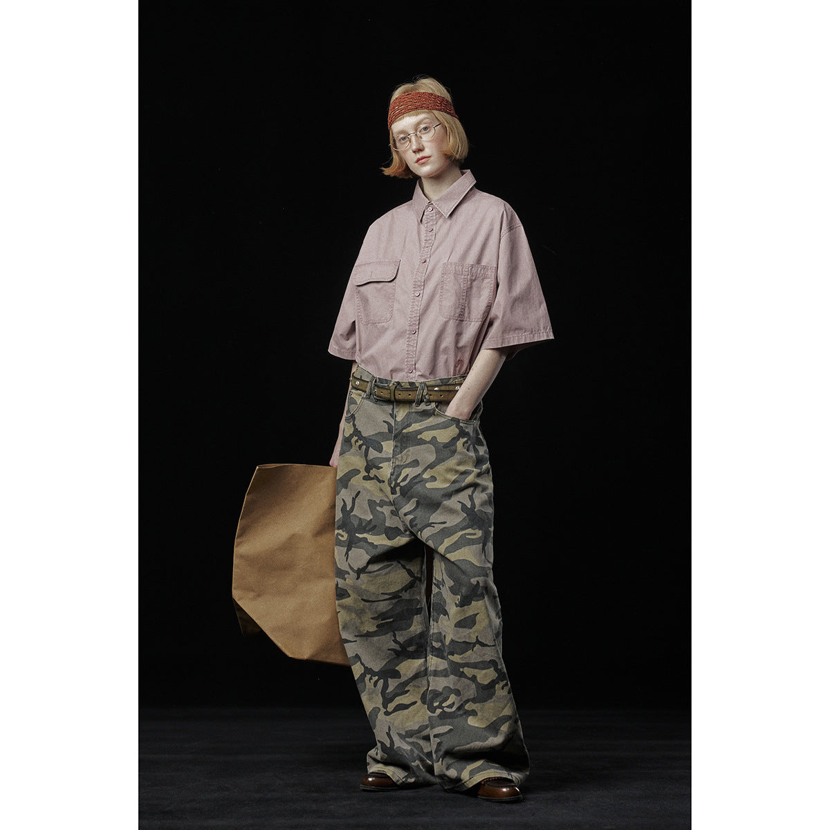 Model wearing a dusty pink short-sleeve button-up shirt and loose camouflage trousers, front view.