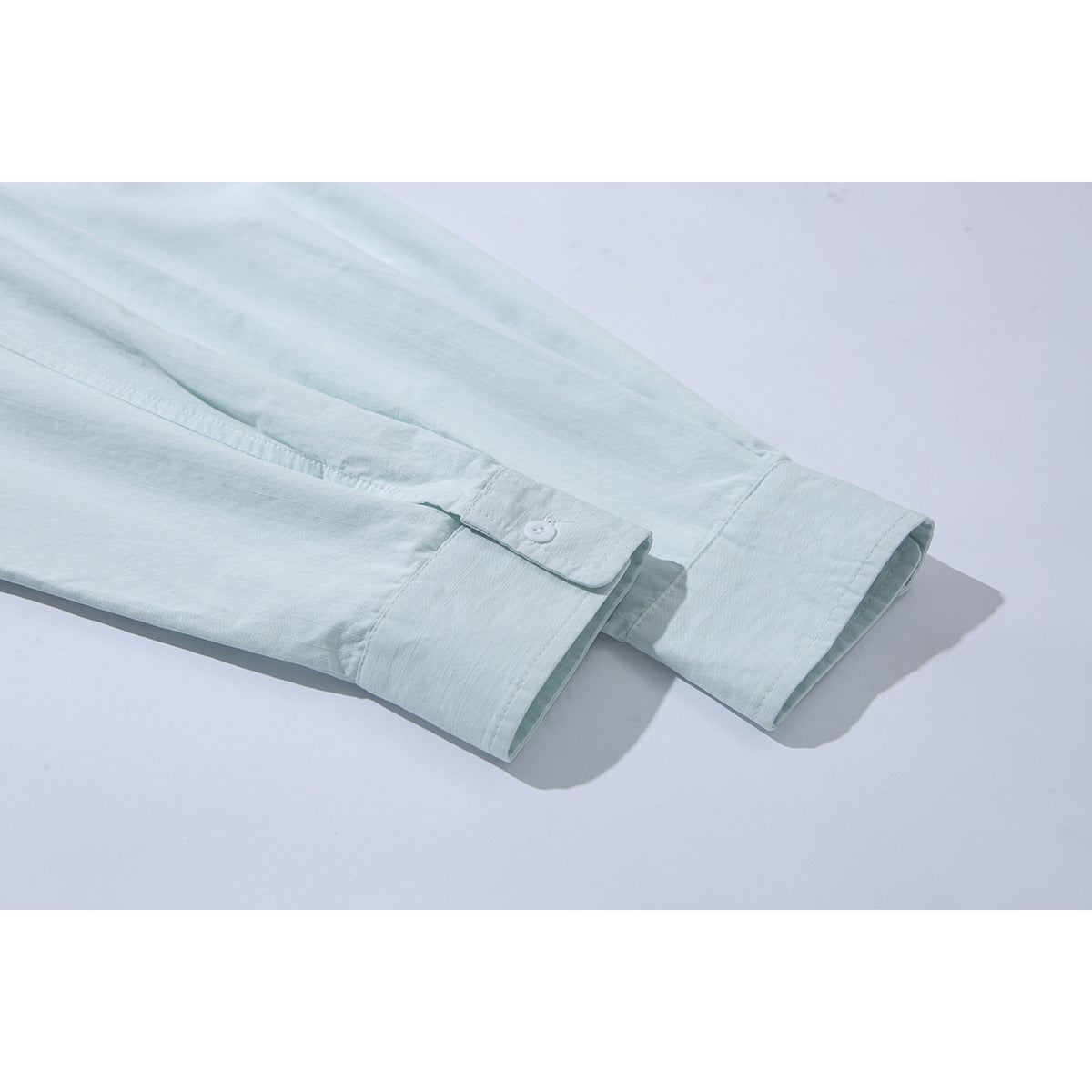 Close-up of the pale mint shirt's long sleeves and buttoned cuffs.