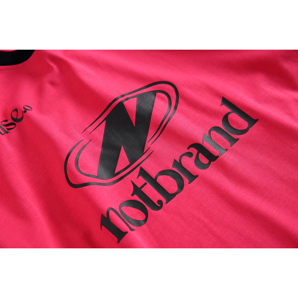 Close-up of black graphic lettering and an oval emblem printed on the bright pink T-shirt.