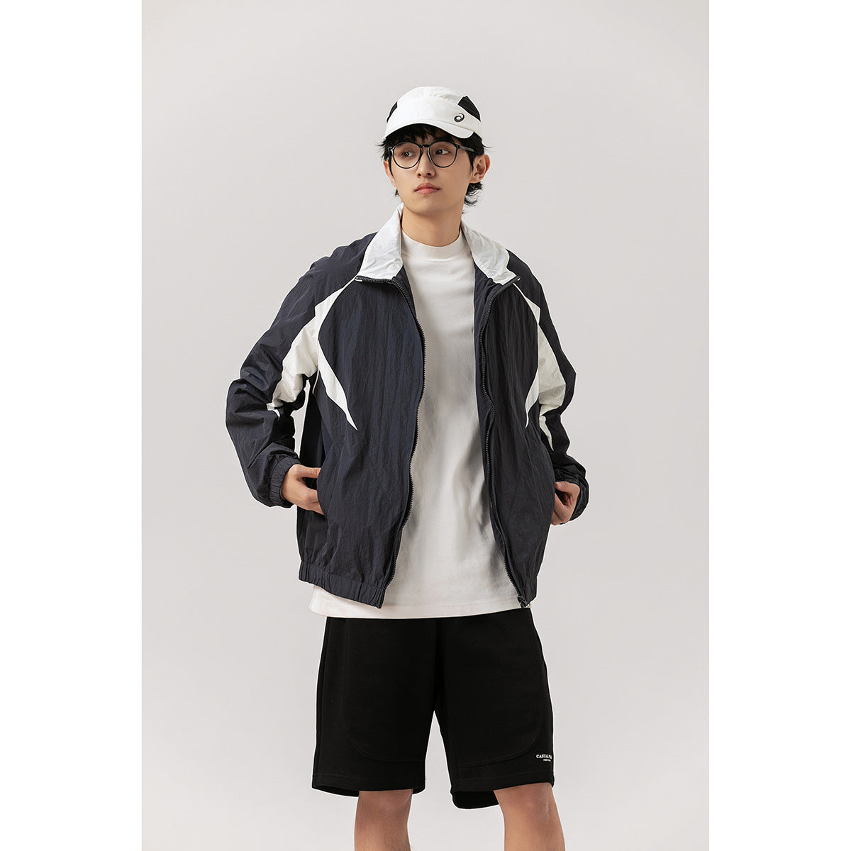 Front view of a model wearing an open black jacket with bold white panels over a white shirt and black shorts.
