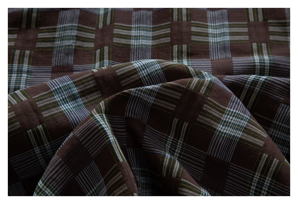 Close-up of dark brown fabric draped in folds, showing a large blue, green, and cream plaid pattern.