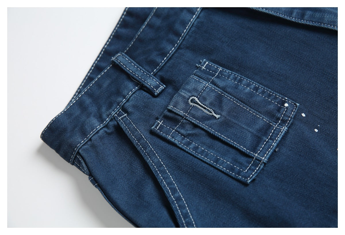 Close-up of a small flap utility pocket and belt loop on dark blue denim shorts, with contrast stitching and white speckles.
