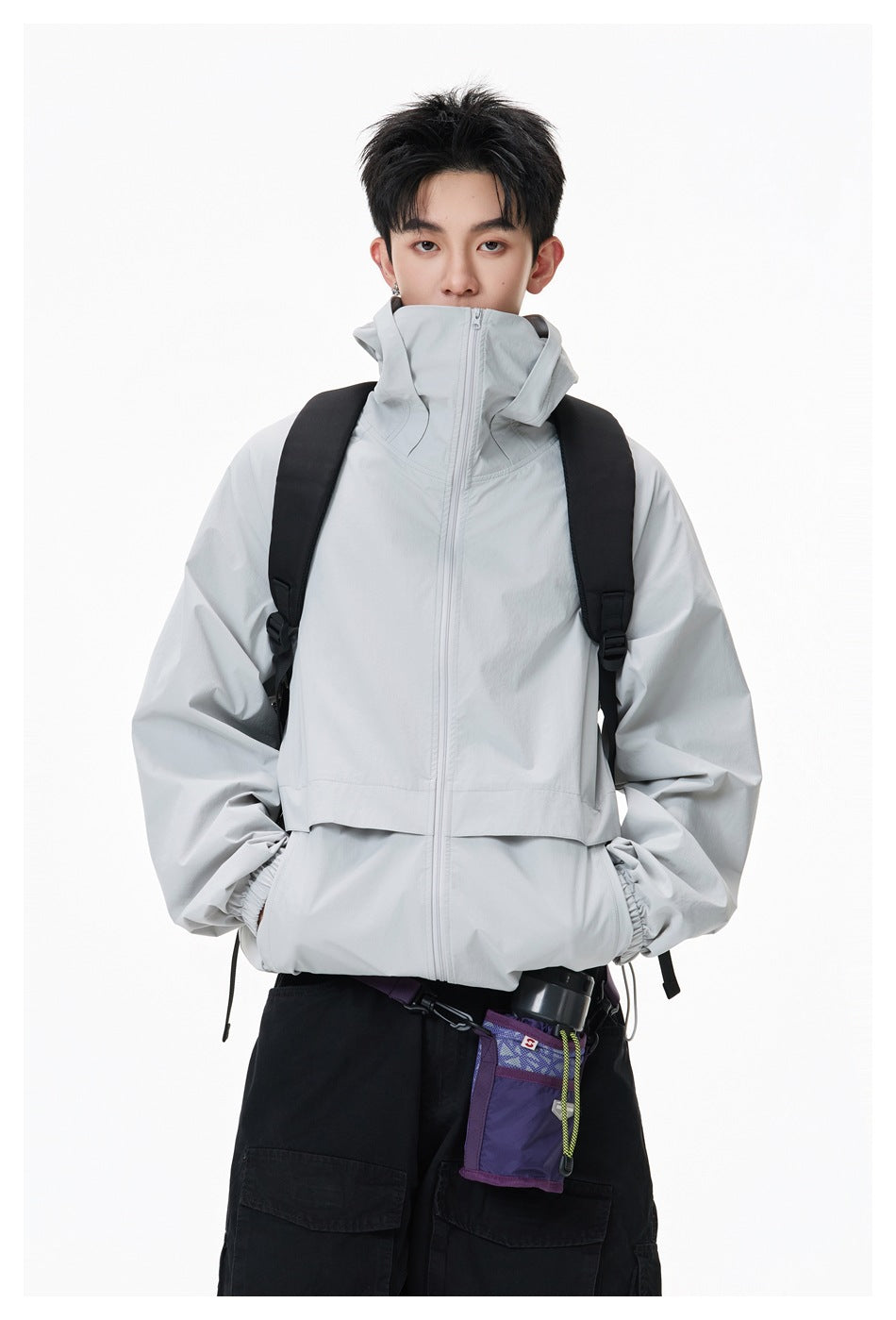 Close view of a model wearing a light gray high-collar zip jacket with a backpack.