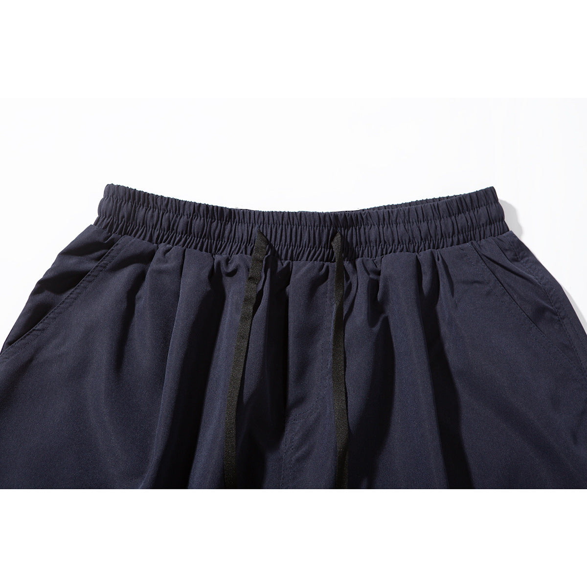 Close-up of navy shorts with an elastic waistband, black drawstrings, and pleated fabric.