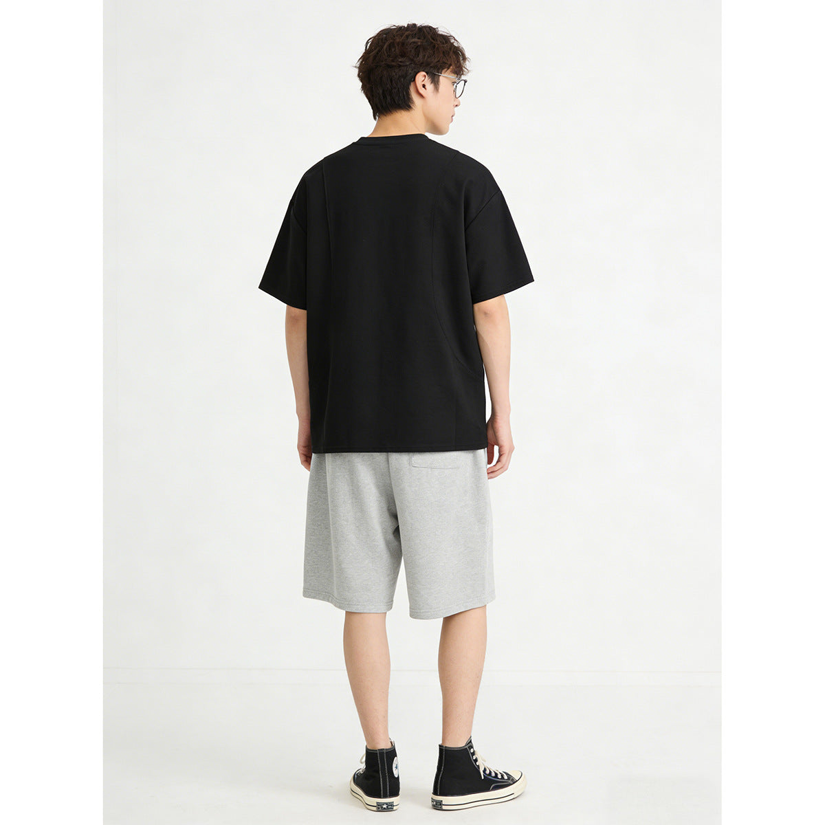 Rear view of a model wearing a black oversized T-shirt and light gray shorts.