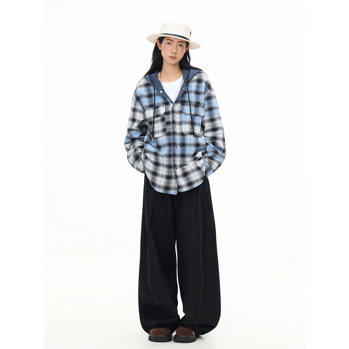 Full-length model wearing a blue-gray plaid hooded button-up shirt with black wide-leg pants and a white hat.