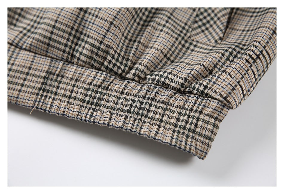 Close-up of a folded edge and stitched seam on a beige, black, and blue plaid garment.