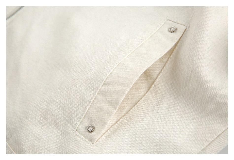Close-up of an ivory textured garment with a diagonal opening and two small silver floral buttons.
