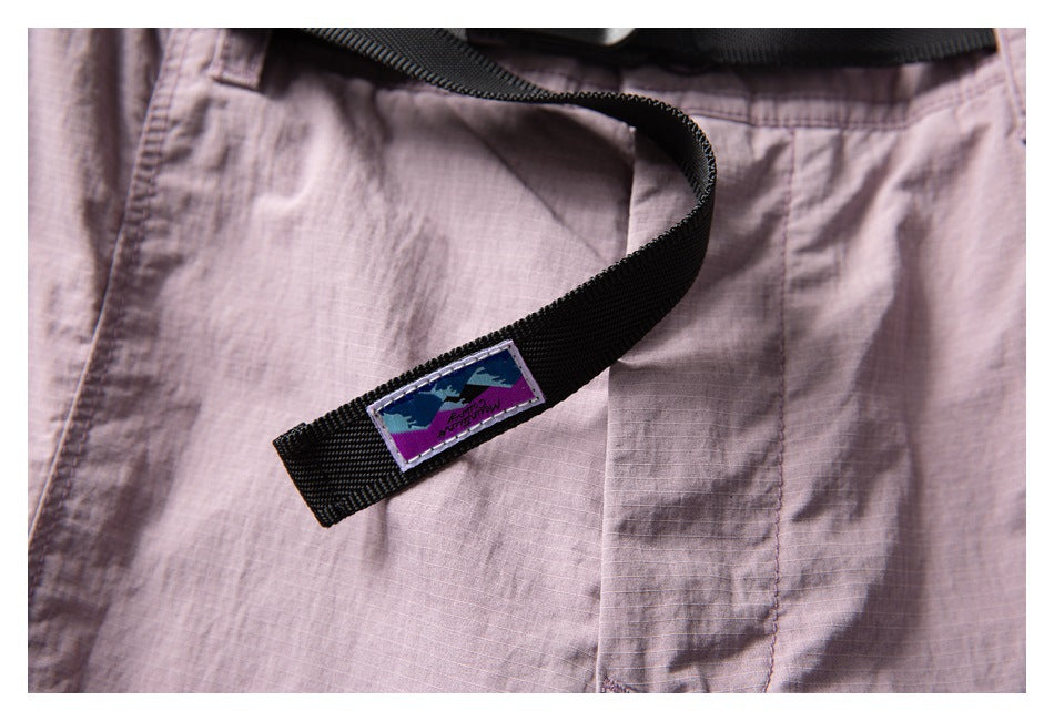 Close-up of a black webbing belt and sewn patch on dusty mauve shorts.
