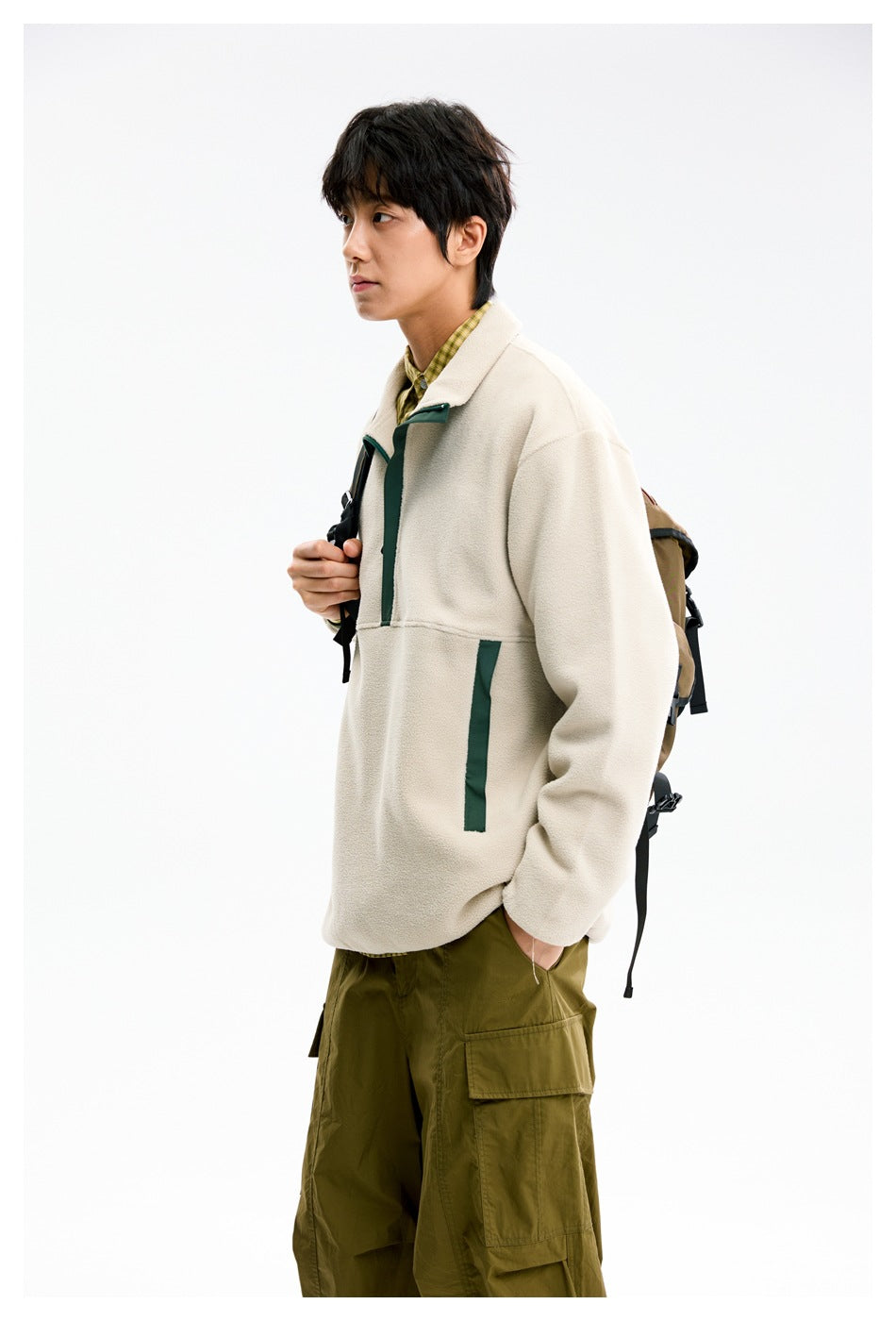 Side view of a model wearing a cream pullover with dark green trim and olive cargo pants, carrying a backpack.