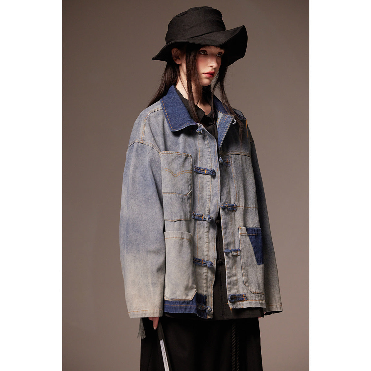 Close front view of a model in a gray denim jacket with dark blue panels, large pockets and frog closures.