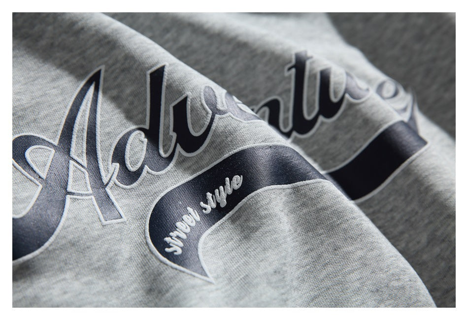 Close-up of raised English lettering and a dark curved graphic on gray sweatshirt fabric.