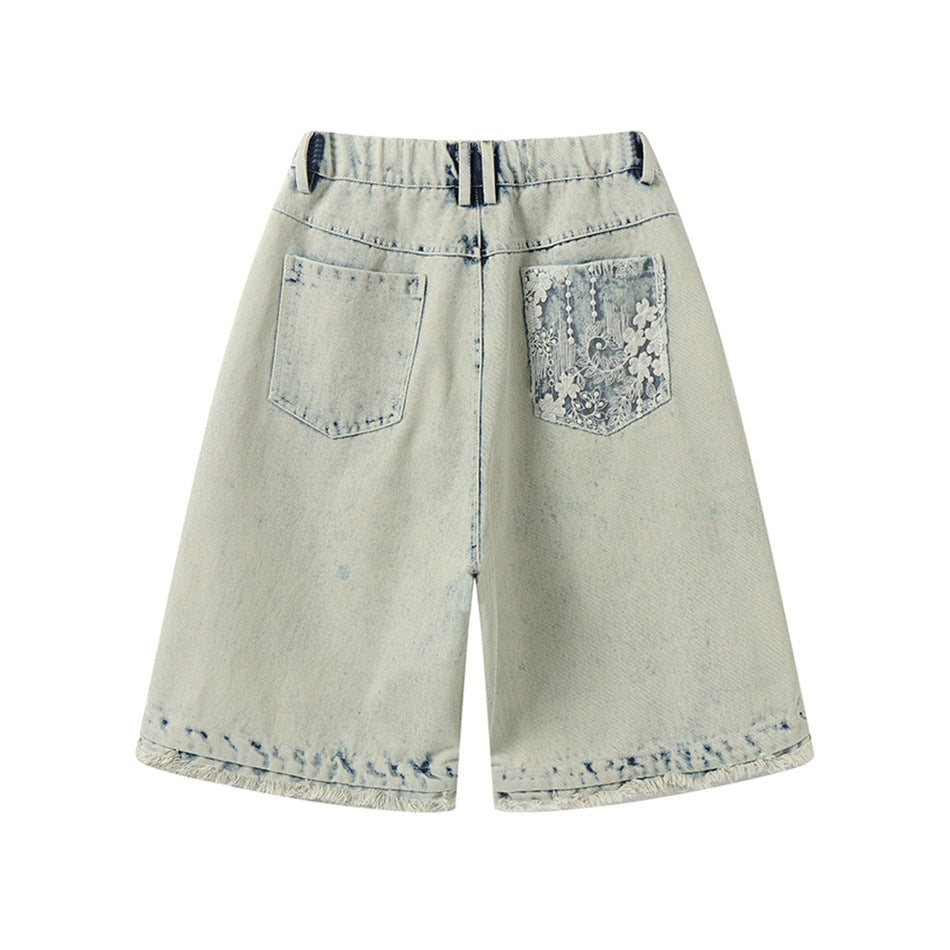 Back view of light blue washed denim shorts with a lace-covered right back pocket and frayed hems