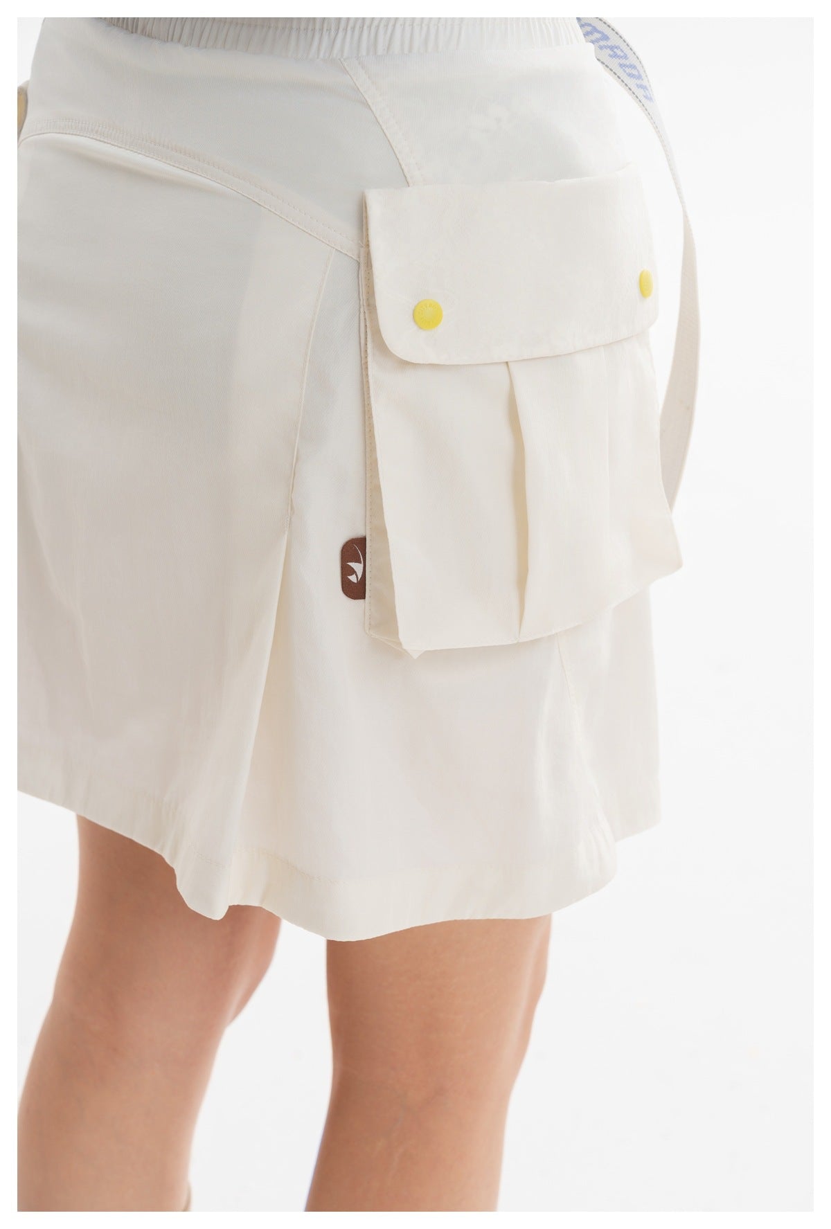 Close-up of the ivory skort's large pleated cargo pocket, yellow snaps, waistband and stitching.