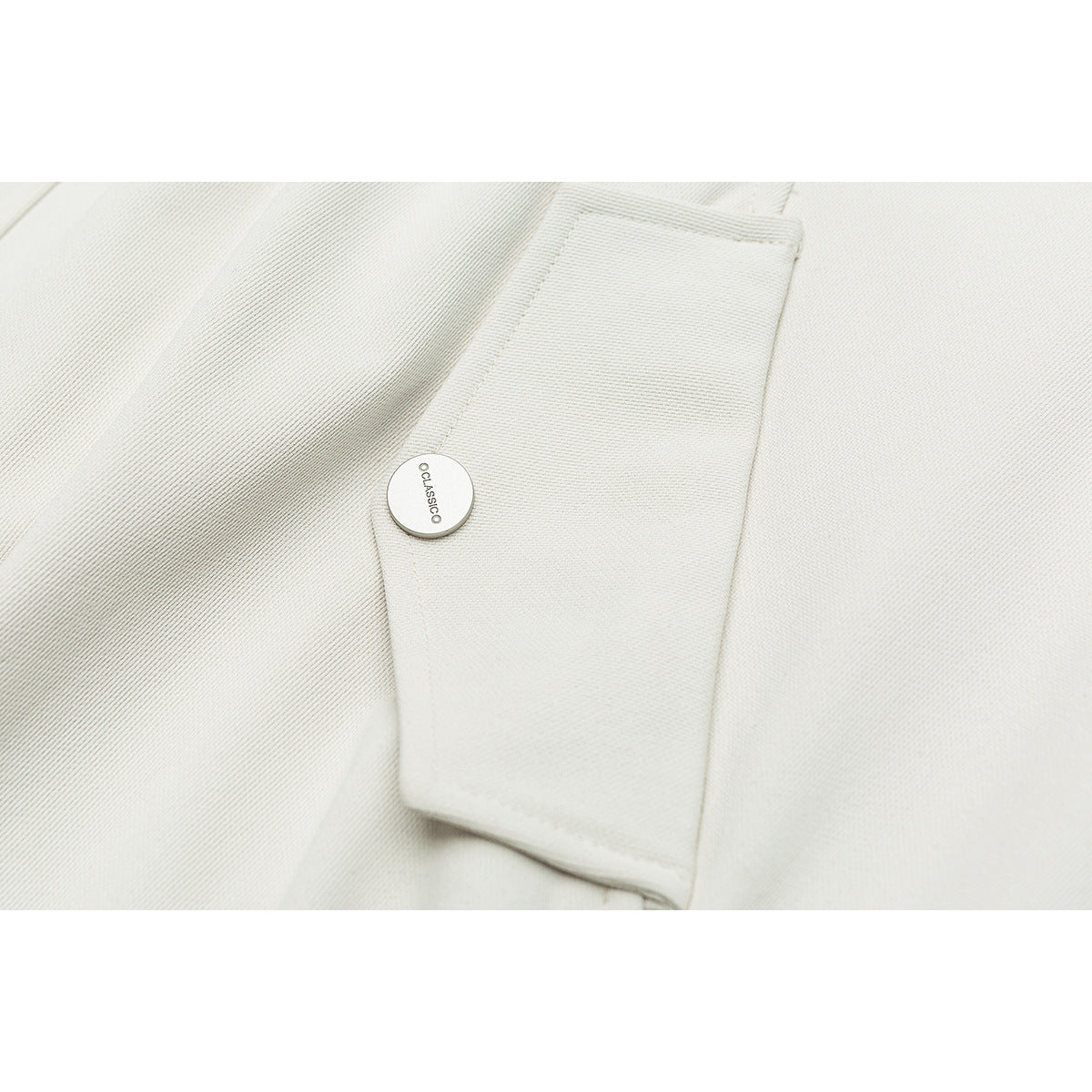 Close-up of an off-white jacket cuff tab with a round metal button and visible stitching.