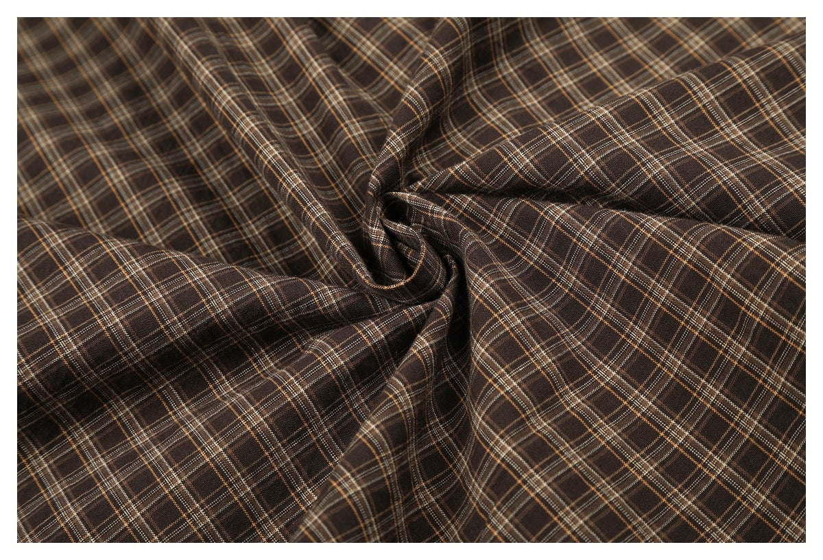 Close-up of brown plaid fabric gathered into folds, showing its checked pattern.