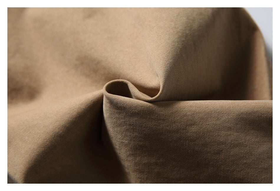 Close-up of tan-brown fabric folded to show its fine diagonal weave and drape.