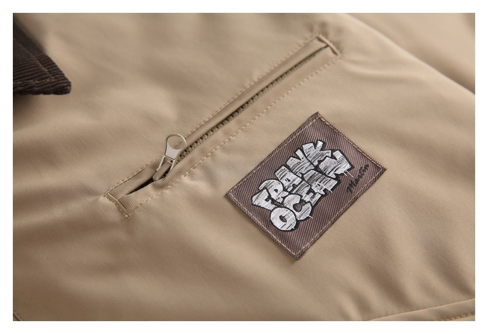 Close-up of a tan jacket showing a slanted zip pocket and a sewn graphic patch.