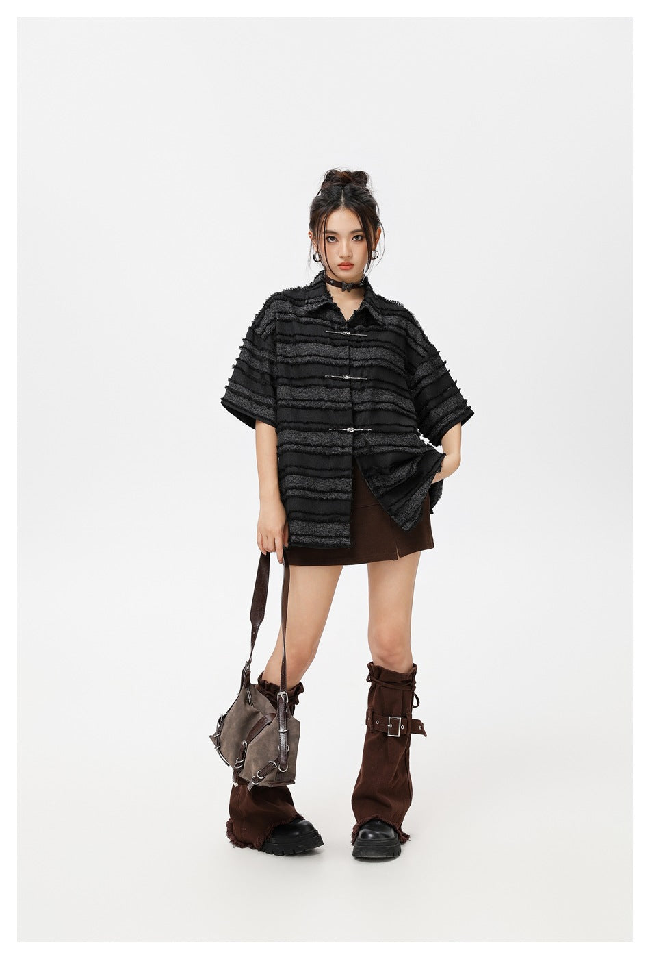 Model wearing an oversized black striped shirt, shown with its front panel open over a brown mini skirt.