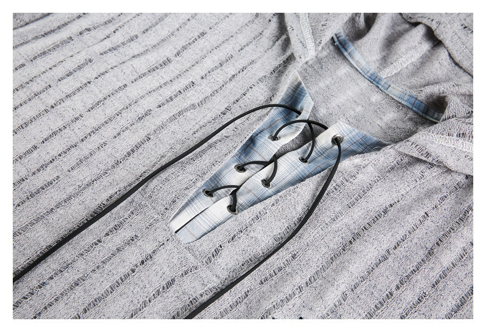 Close-up of a gray textured top with openwork stripes, a blue plaid inset at the neckline, and black lacing.