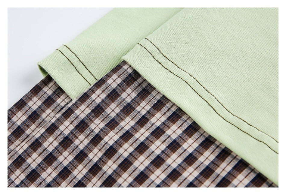 Close-up of pale green fabric with dark stitching layered over brown, navy, and cream plaid fabric.
