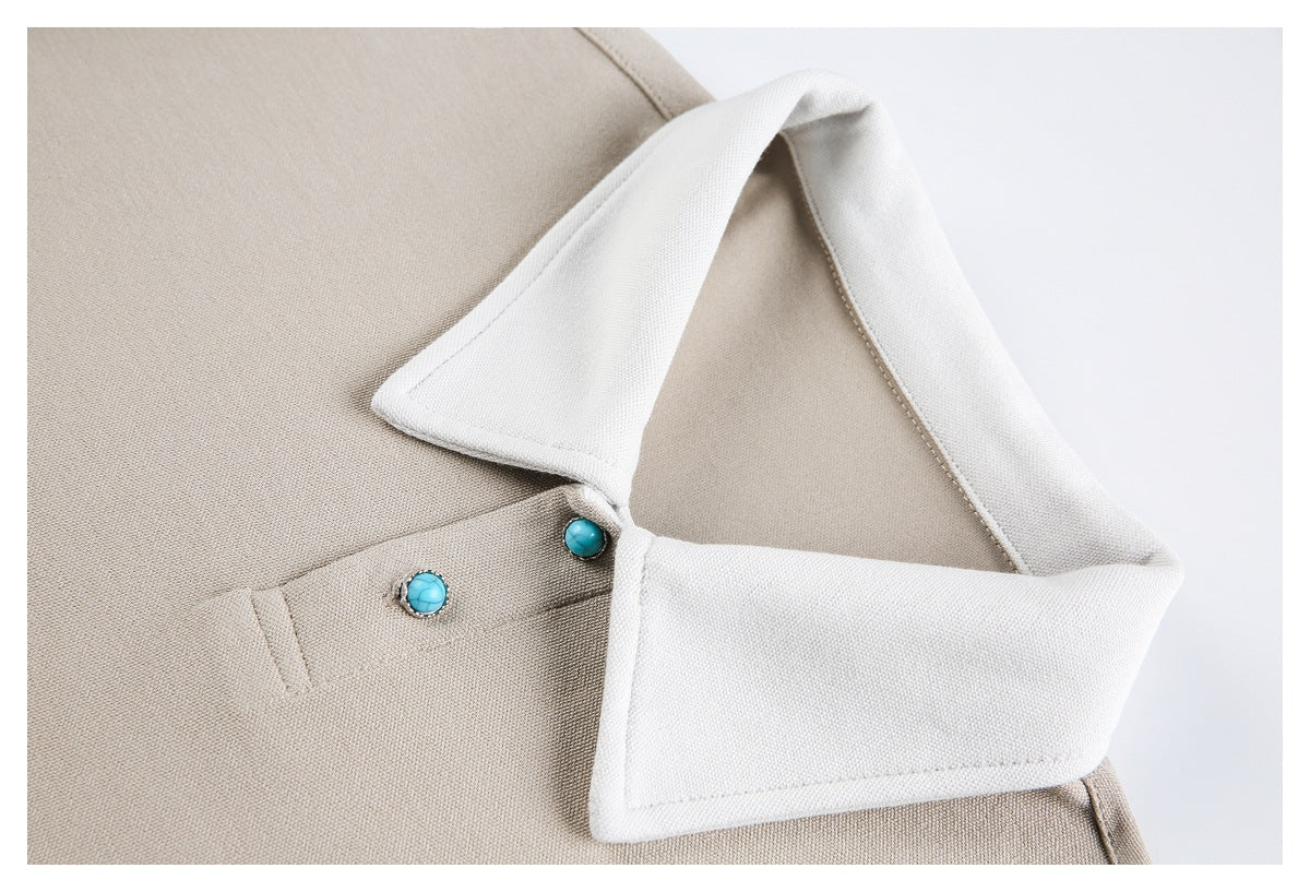 Beige garment close-up showing a wide white collar, placket, and turquoise buttons.