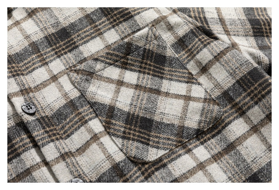 Close-up of a patch pocket and black buttons on a cream, gray, and brown plaid shirt.