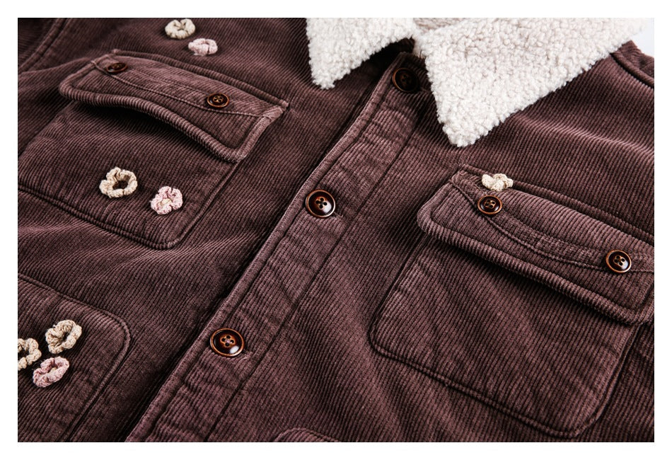 Close-up of a plum-brown ribbed jacket front with cream sherpa collar, brown buttons, flap pockets and small crochet flowers.