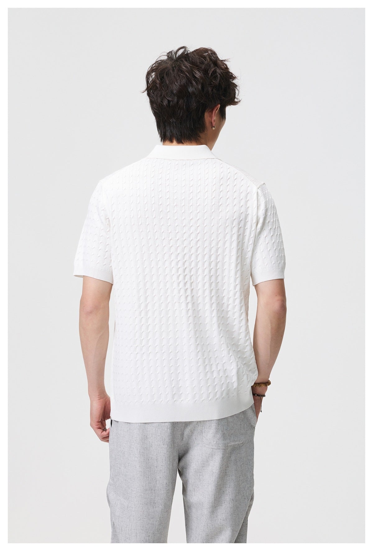 Back view of a model wearing a white short-sleeve cable-knit polo with ribbed collar, cuffs, and hem.