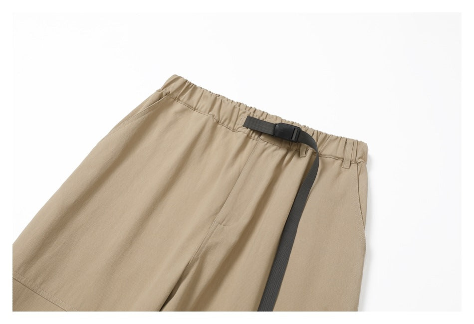 Close-up of tan pants with an elastic waistband, belt loops, and a dark adjustable webbing belt.