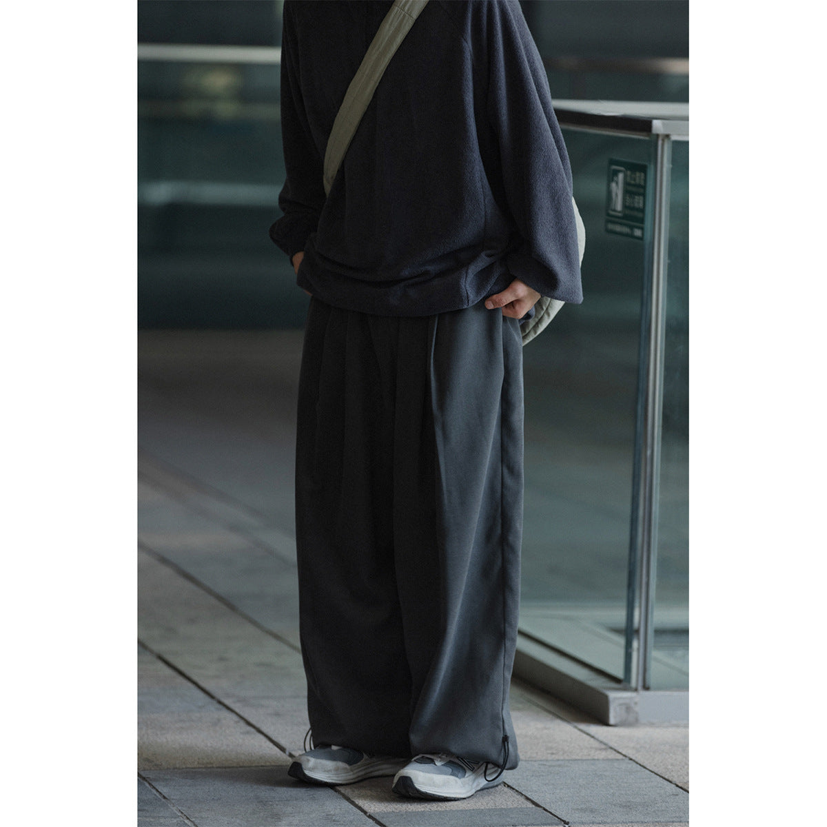 Cropped view of a person wearing a dark navy oversized top and charcoal wide-leg pants with adjustable ankle cords.