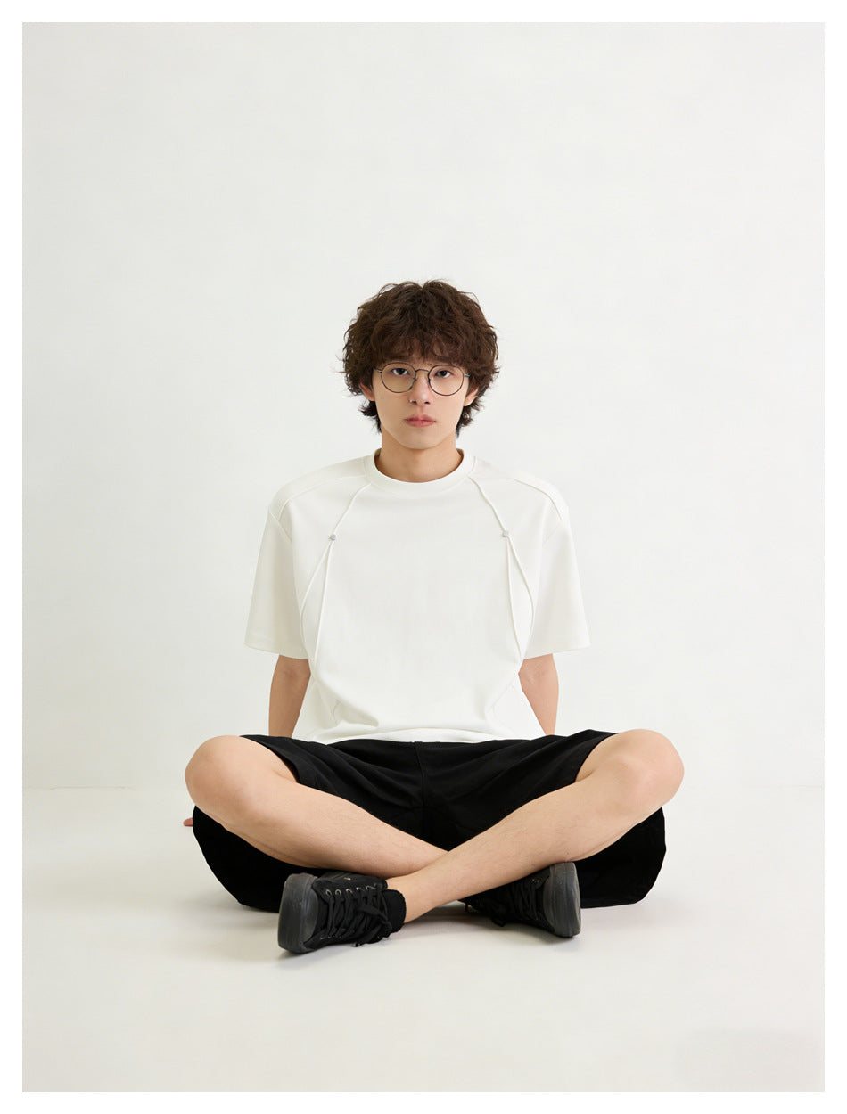 Model seated cross-legged wearing an oversized white short-sleeve tee with curved front panels and small snaps.