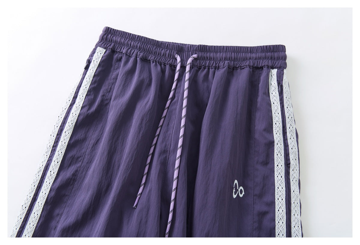 Close-up of the purple pants' elastic drawstring waist, white lace side stripes, and small emblem.