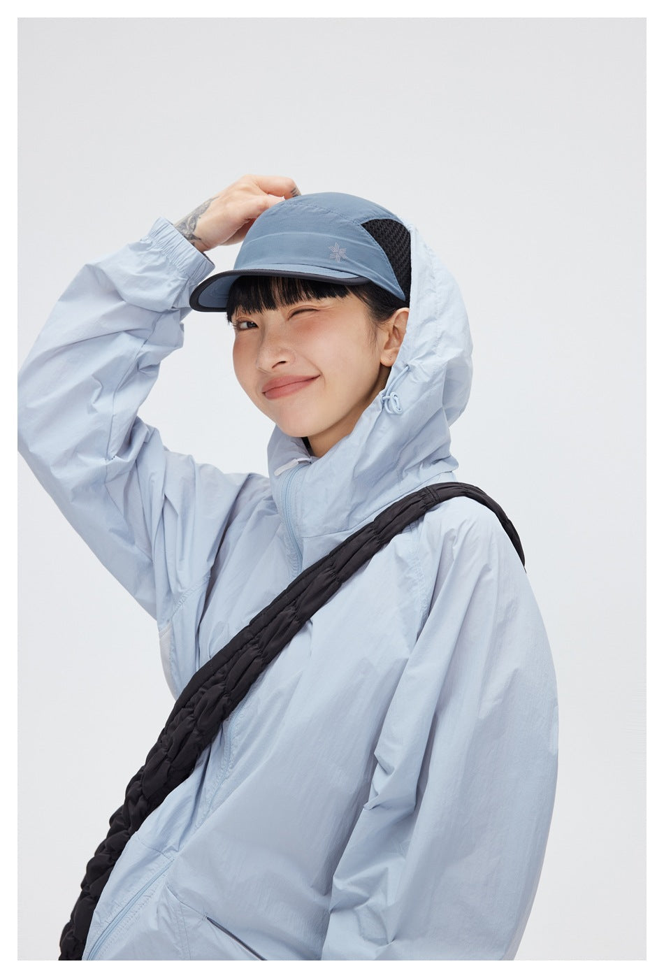 Close view of a model in a pale blue hooded jacket and blue cap with a black mesh side panel.