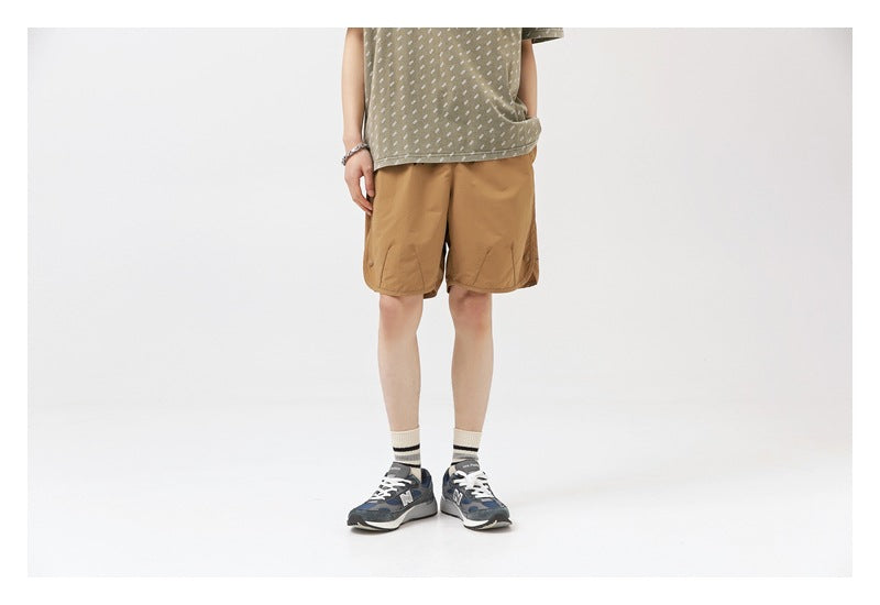 Model wearing tan knee-length shorts with side pockets and a patterned olive shirt.