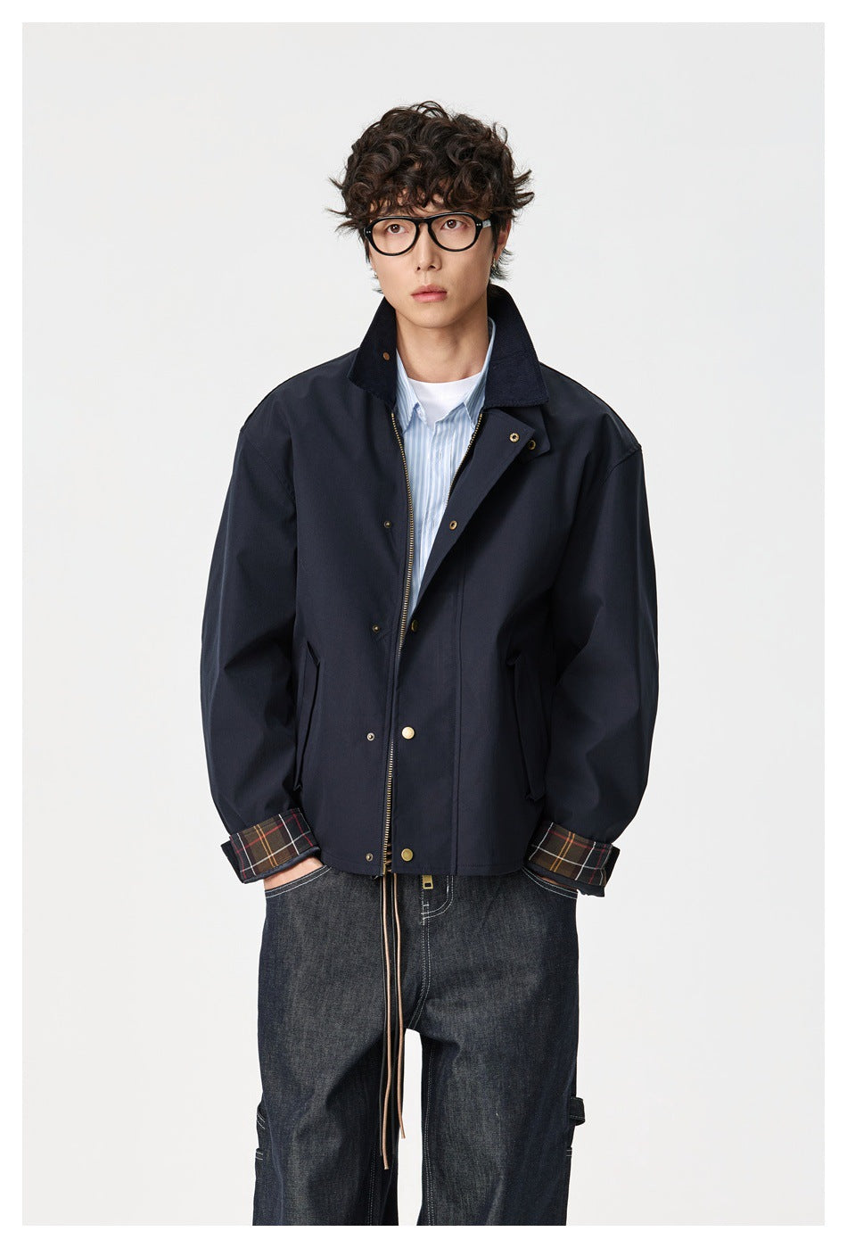 Front view of a model wearing a dark navy jacket with a corduroy collar, brass hardware and plaid cuffs.