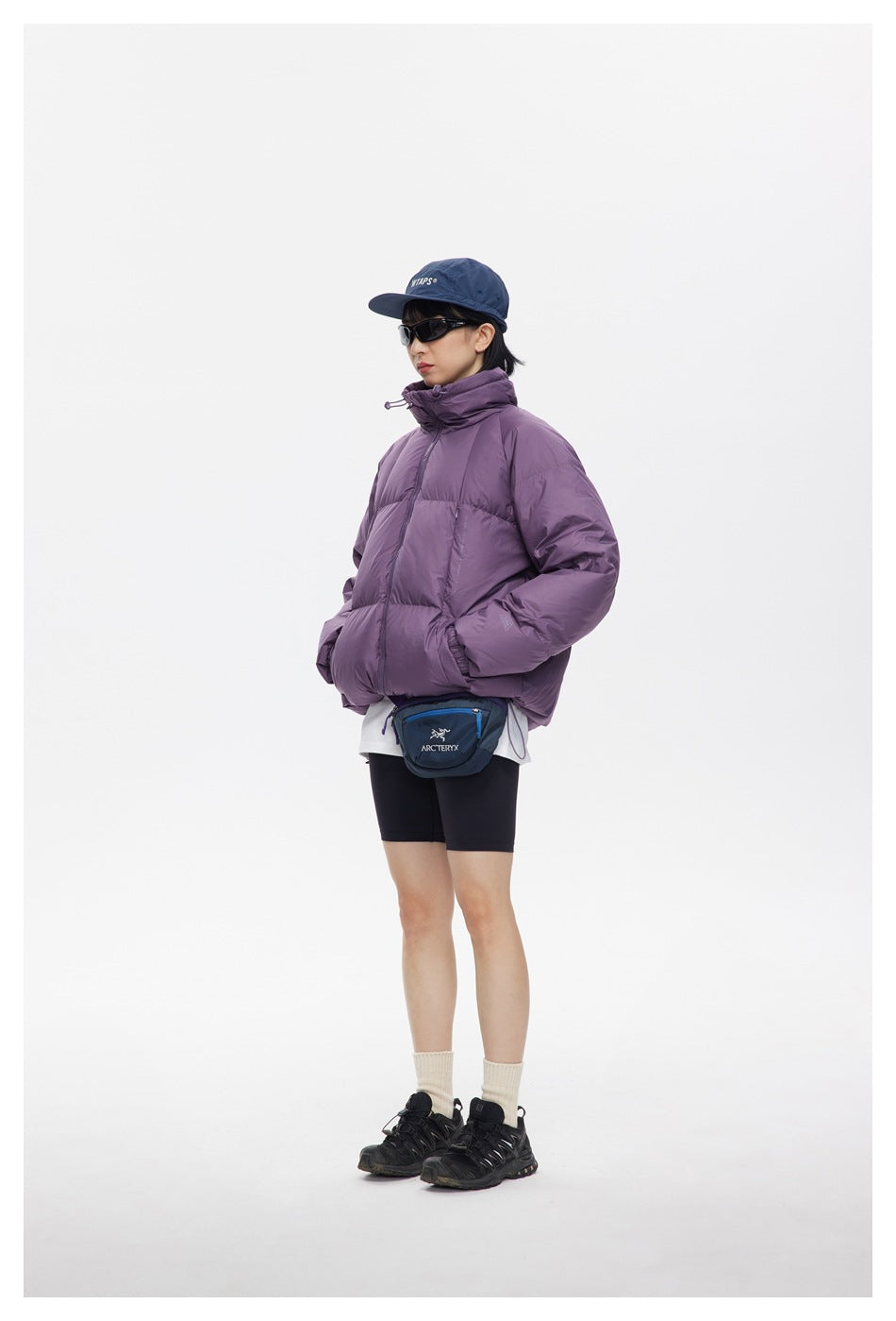 Model wearing a plum-purple quilted puffer jacket with a high collar, shown from a three-quarter front angle.